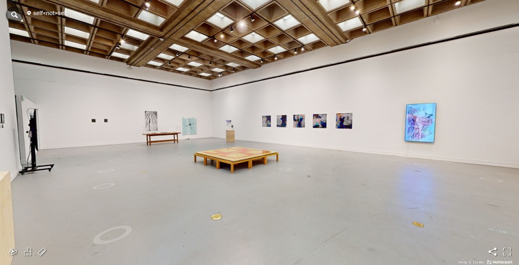 An art gallery with multiple works hanging on the walls in the distance and a yellow/red sculpture in the middle of the floor